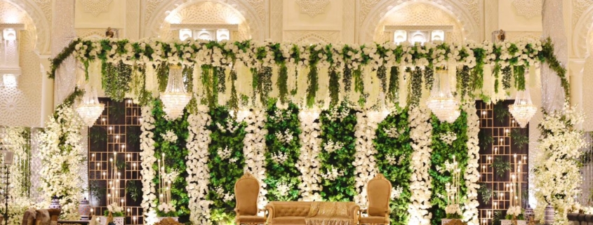 Luxurious wedding stage at Dehleez Banquet decorated with white flowers, greenery, chandeliers, and elegant seating.