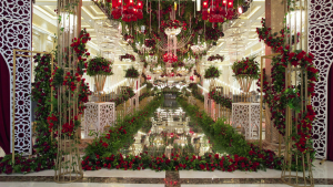 A lavishly decorated wedding stage adorned with red and white flowers, crystal chandeliers, and elegant golden structures, creating a grand and romantic ambiance.