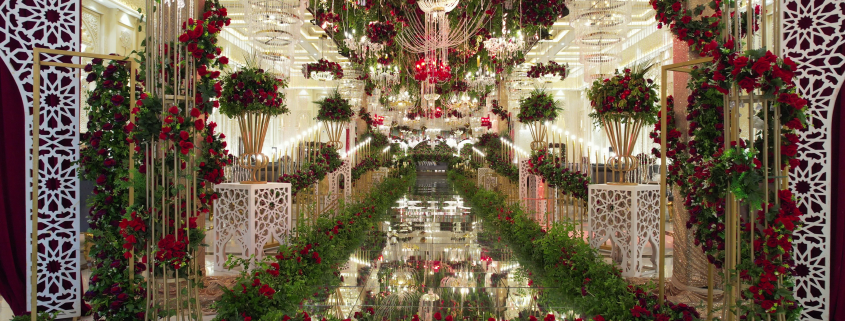A lavishly decorated wedding stage adorned with red and white flowers, crystal chandeliers, and elegant golden structures, creating a grand and romantic ambiance.